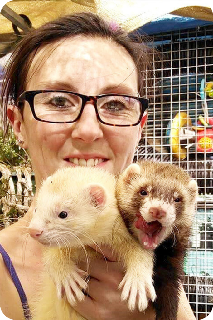 Carina Smith smiles at the camera, holding two ferrets in her hand.