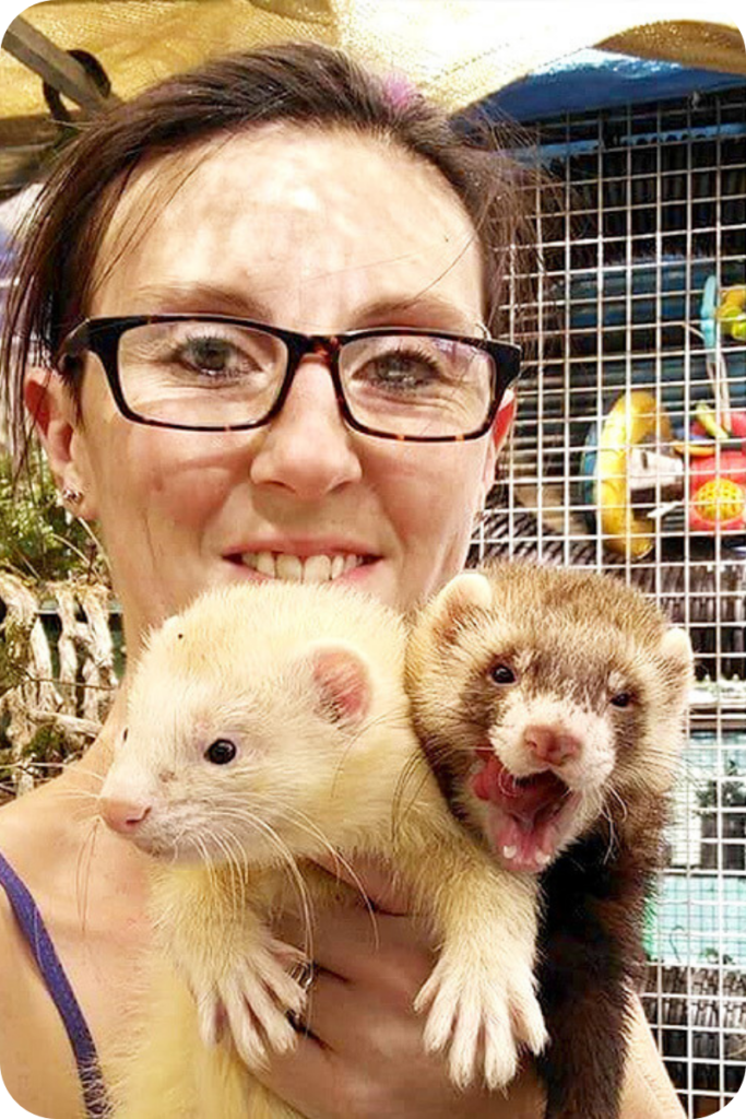 Carina Smith smiles at the camera, holding two ferrets in her hand. 