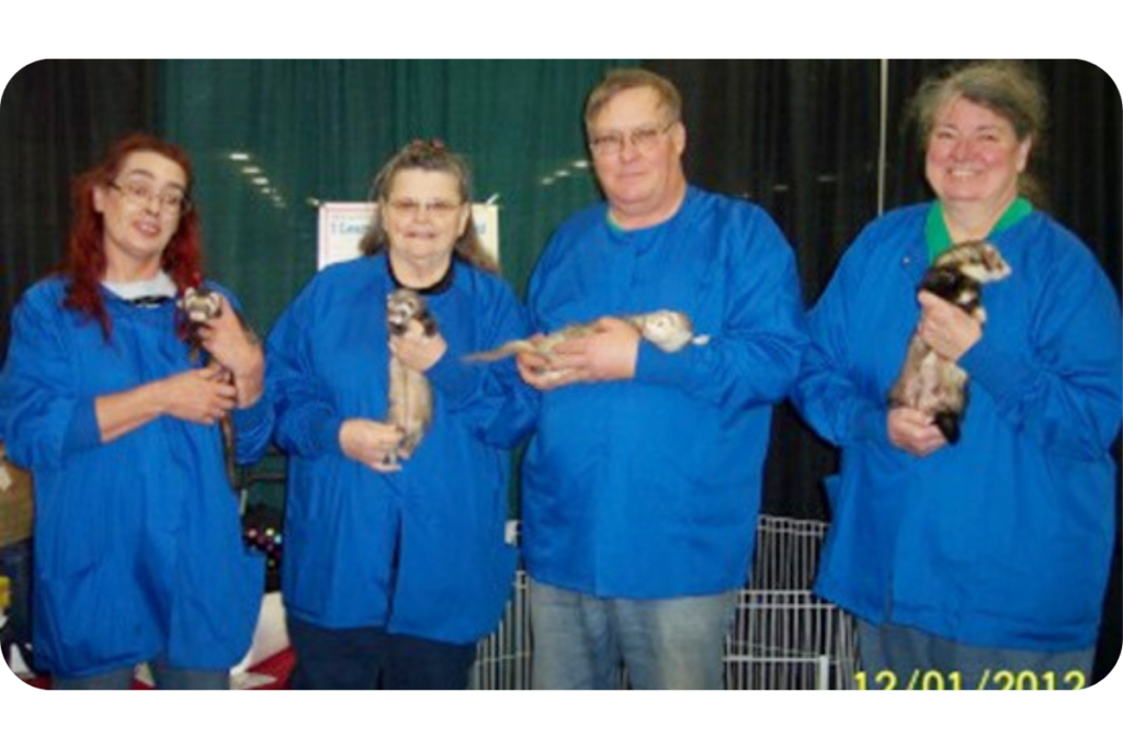 A group of four people wear matching blue shirts and cradle ferrets in their arms.