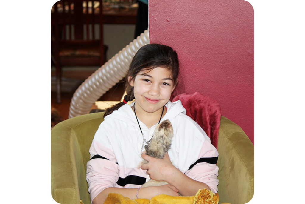 A child sitting with a ferret in their lap on a sofa.